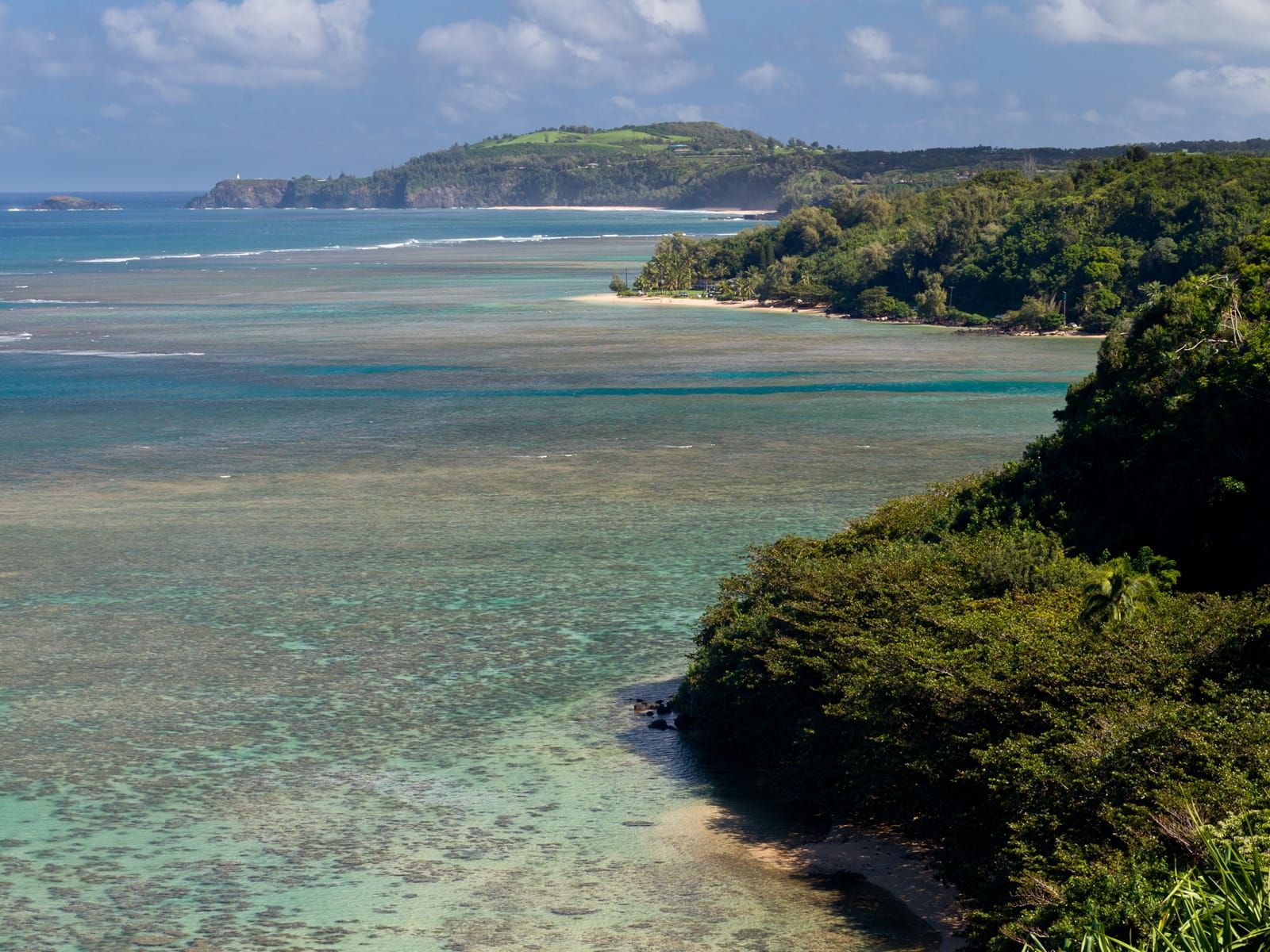 Clear turquoise water over the reef at Anini, with green bluffs beyond