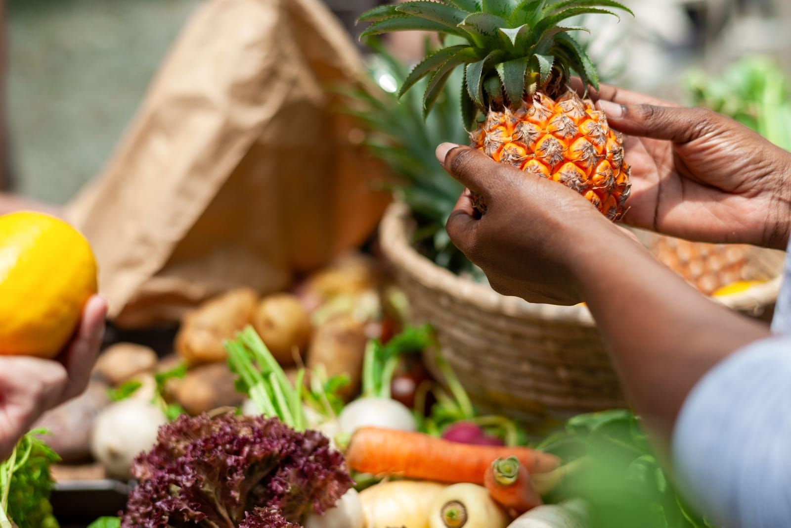Hands holding a pineapple over baskets of fresh produce at an outdoor market