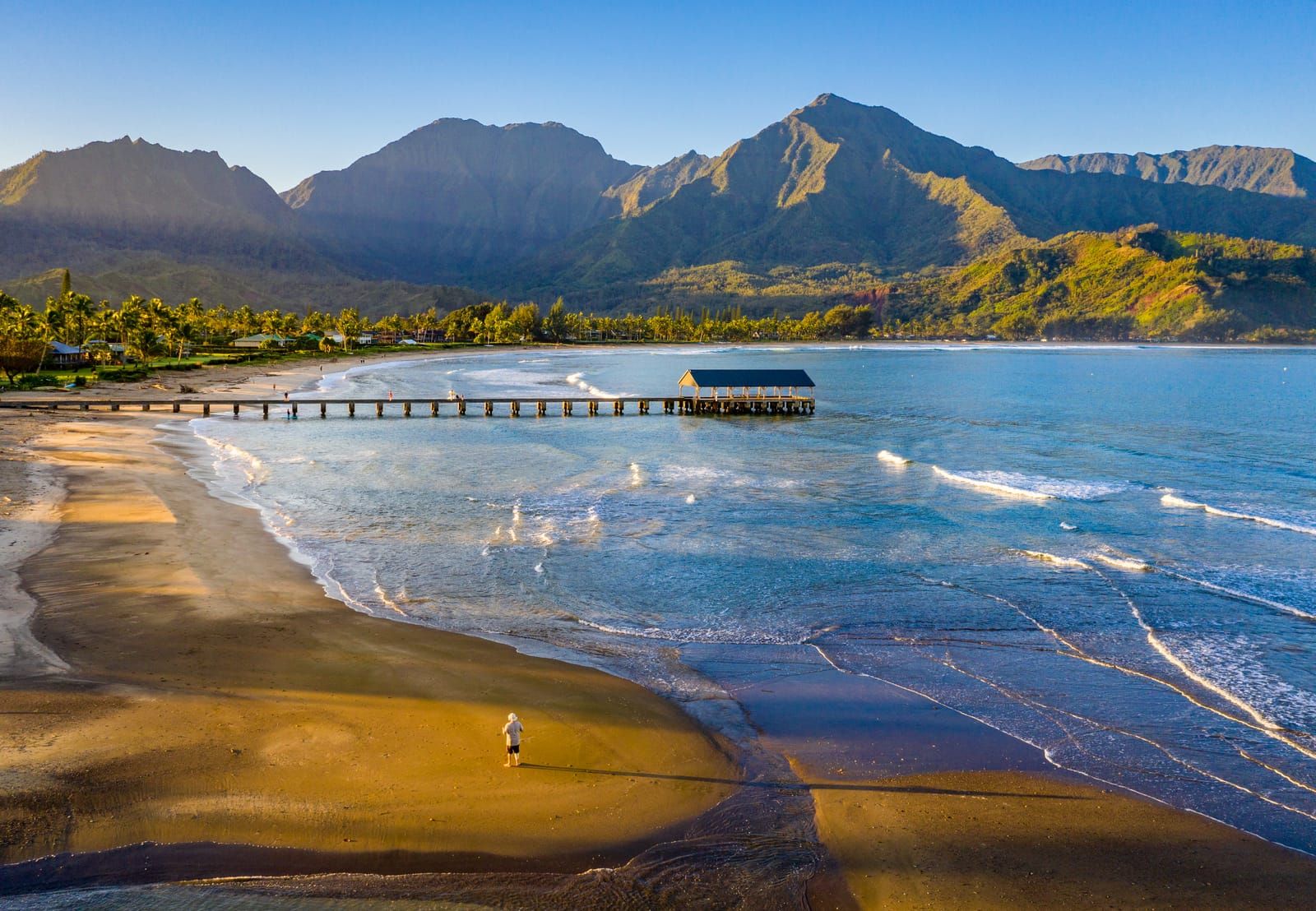 Hanalei Bay at sunrise from above, the pier and golden sand below green mountains