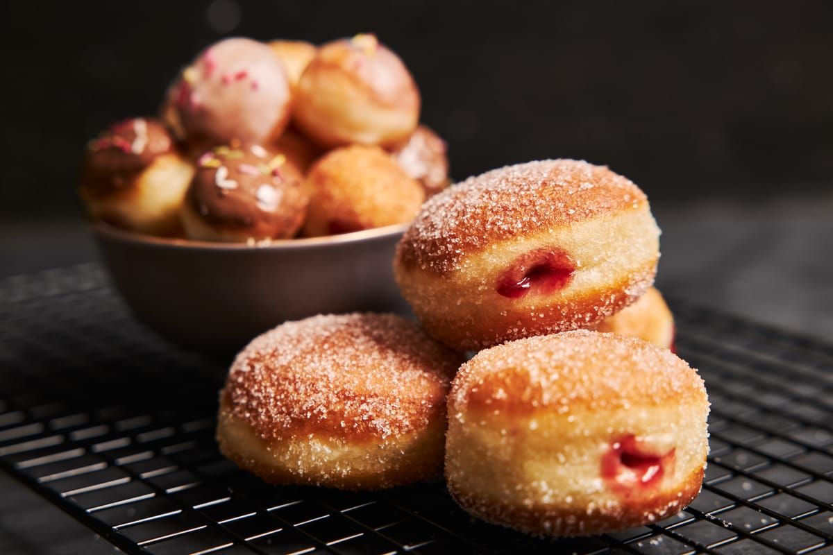 Sugar-coated fried doughnuts, like malasadas, on a cooling rack