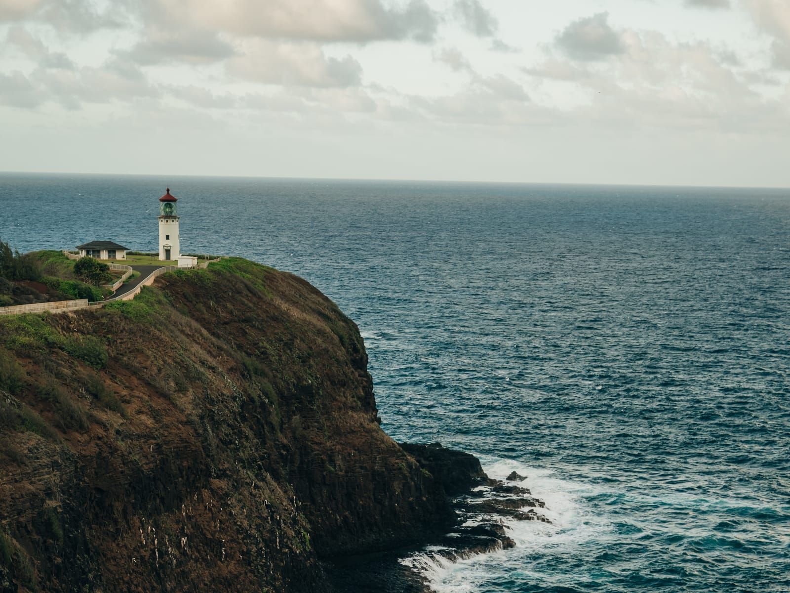 The white Kīlauea Lighthouse on a clifftop above a churning blue sea