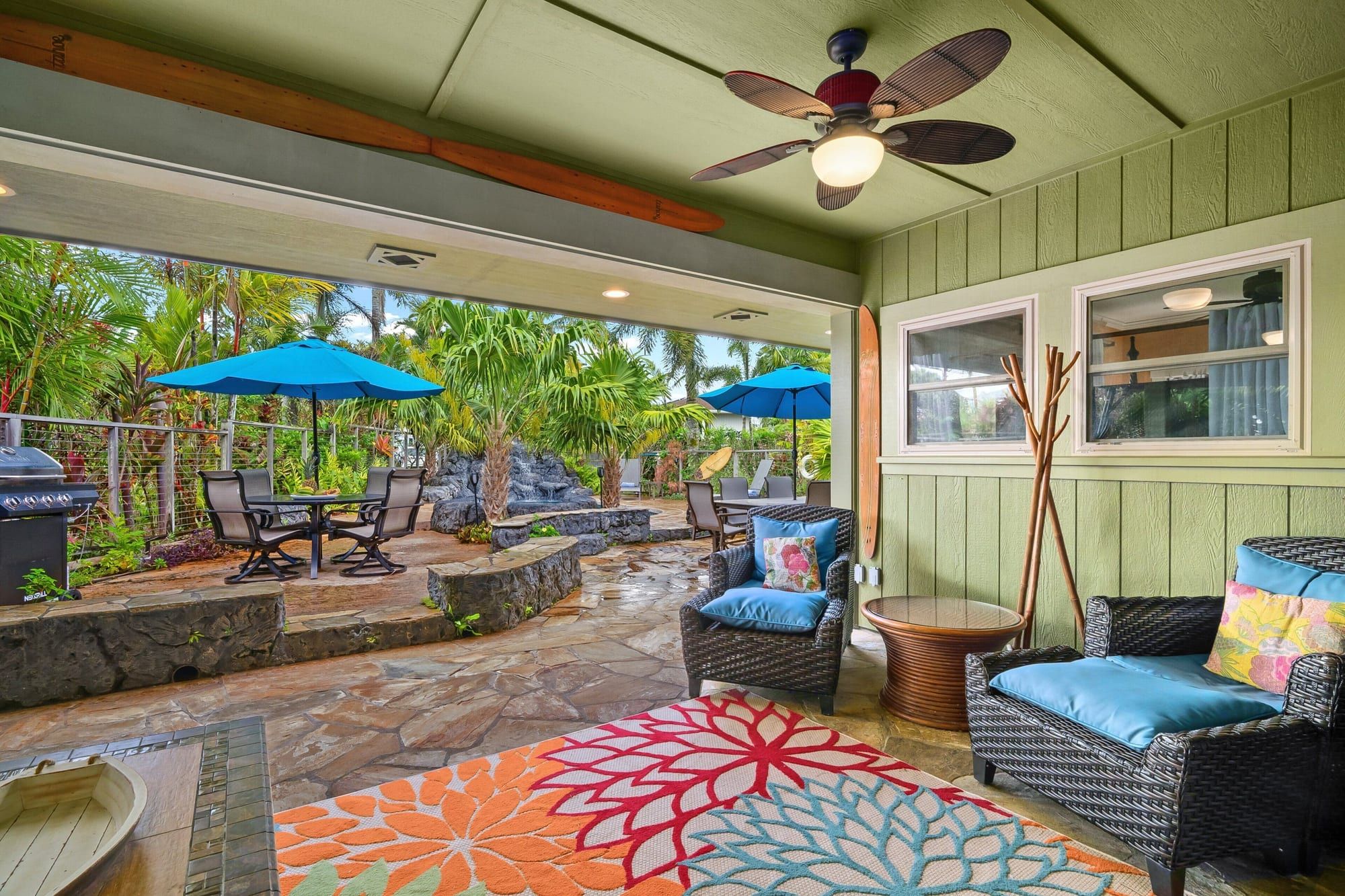 The covered lanai with blue armchairs, a bright rug and the garden beyond