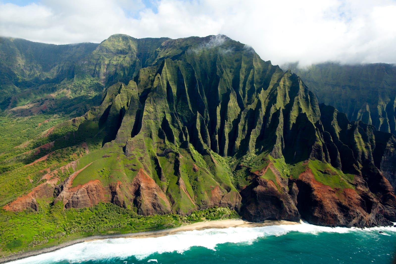 The fluted green cliffs of the Nā Pali Coast above a white-sand beach