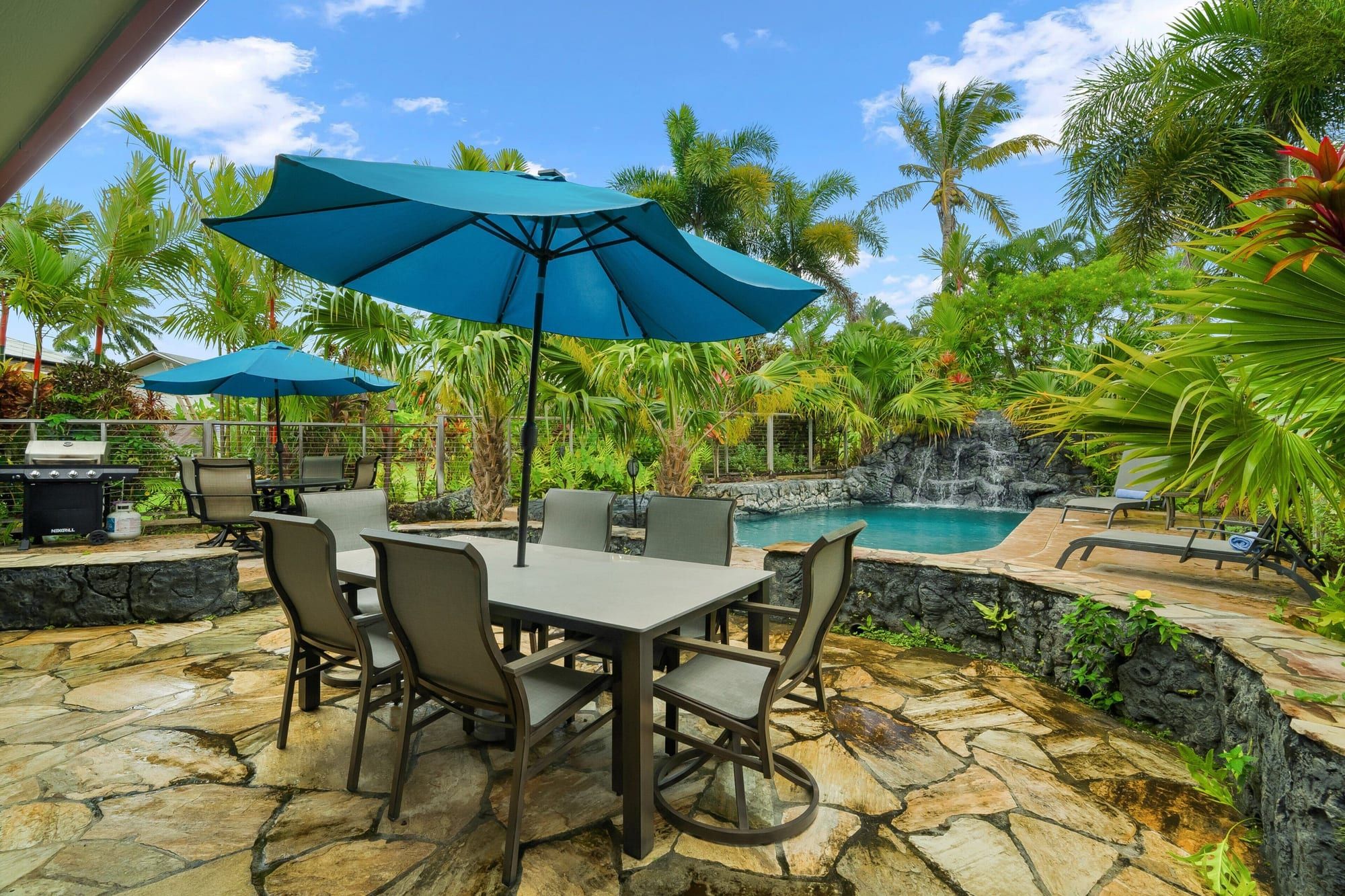 Outdoor dining table under a blue umbrella beside the pool