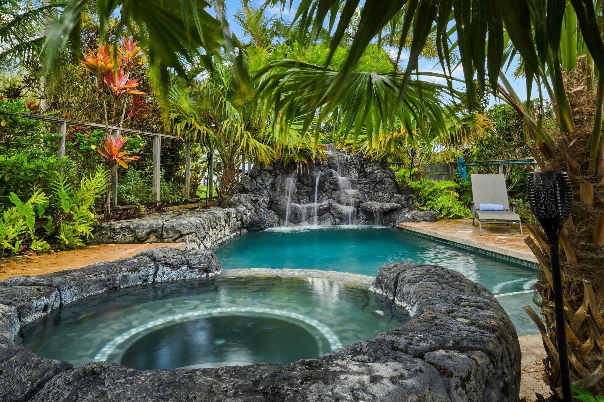 The saltwater pool and round spa, with a lava-rock waterfall and palms behind
