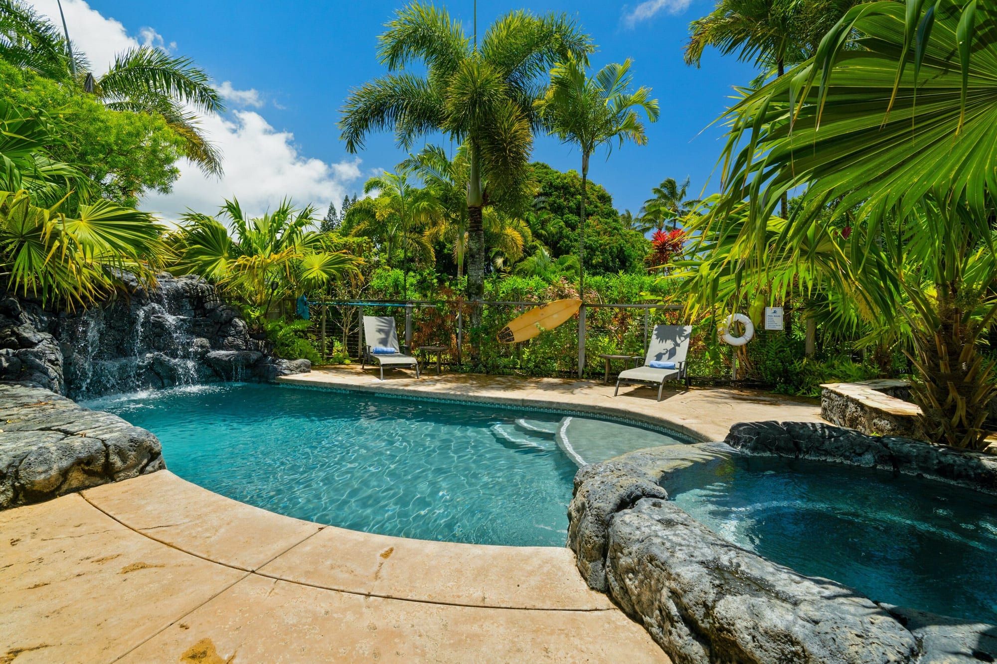 The pool and spa under palms with lounge chairs along the edge