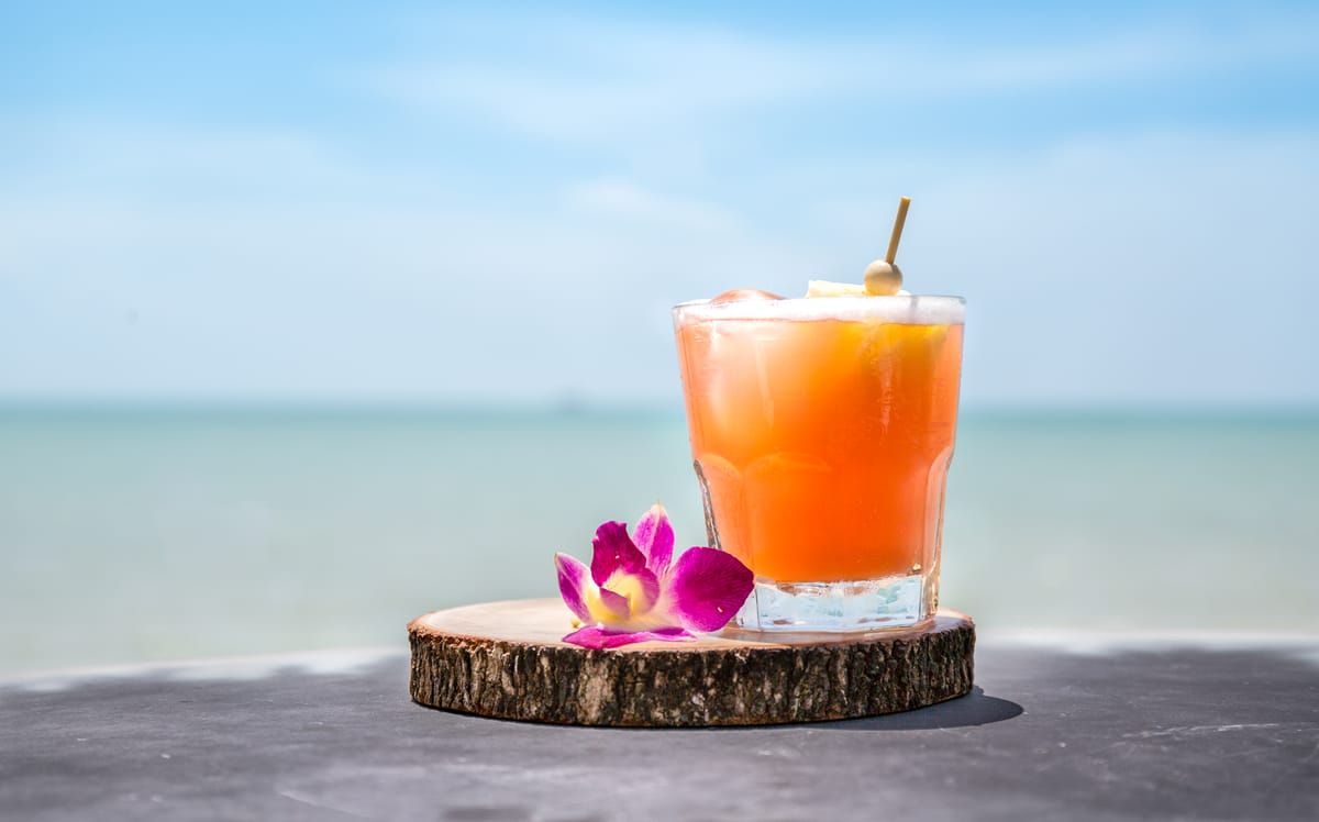 A mai tai with an orchid on a bar table by the ocean